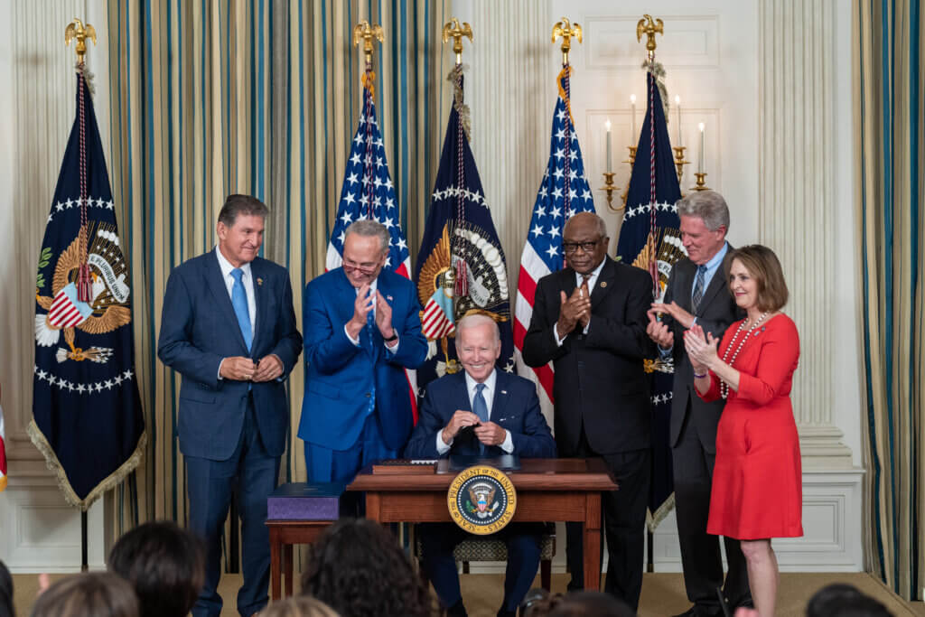 President Joe Biden sitting at a table in the State Dining Room of the White House surrounded by government officials. 