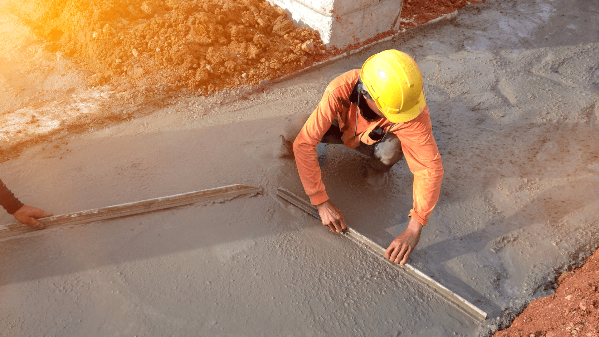 A construction worker levels concrete with trowels.